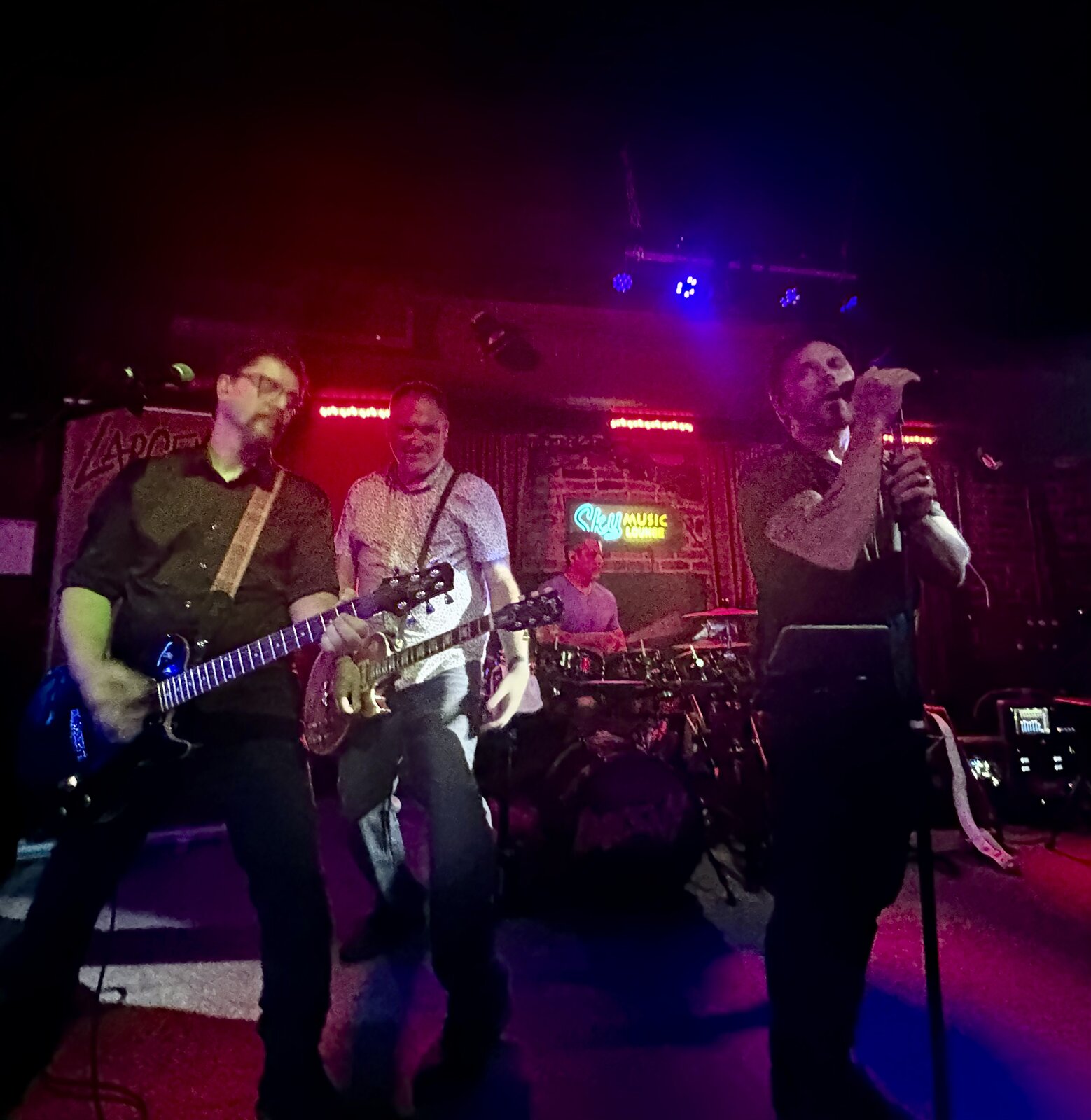 Larceny guitarists Dan and Kevin with vocalist Erik under red and blue lights at Sky Music Lounge